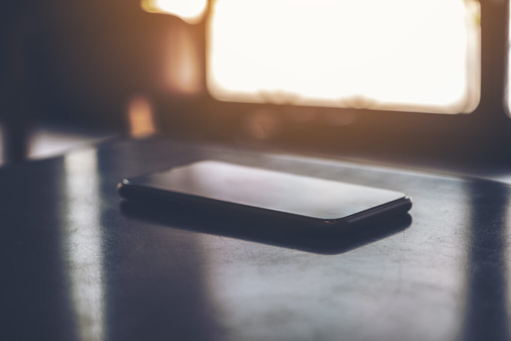 Un smartphone posé face contre la table de nuit, à côté d'une lampe de chevet diffusant une lumière douce et tamisée.