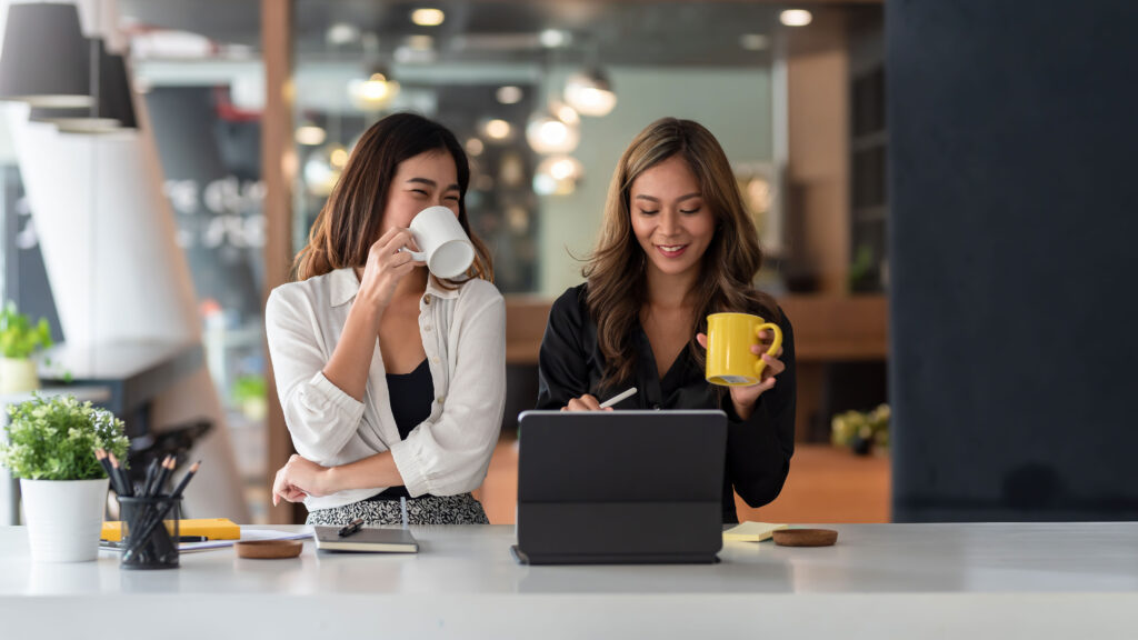 Deux personnes assises à une table, l'une aidant l'autre dans une ambiance détendue avec un café et quelques papiers.