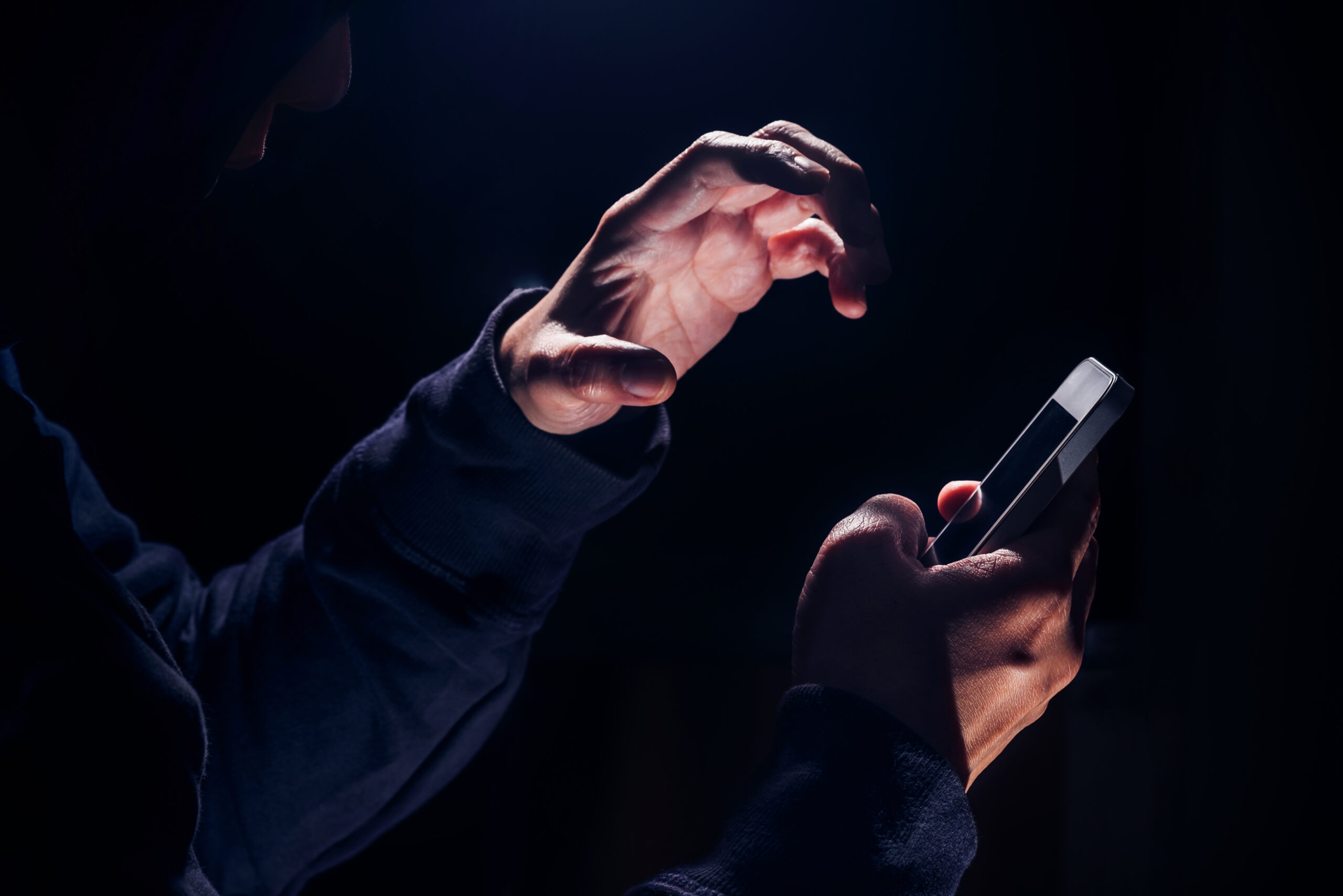 Personne dans le noir de sa chambre, le visage éclairé uniquement par la lumière bleue de son smartphone.