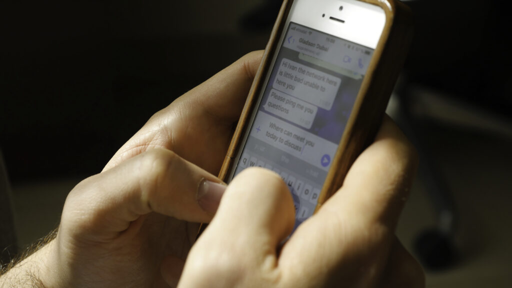 Gros plan sur des doigts tapant sur le clavier d'un smartphone, avec une interface de discussion épurée.