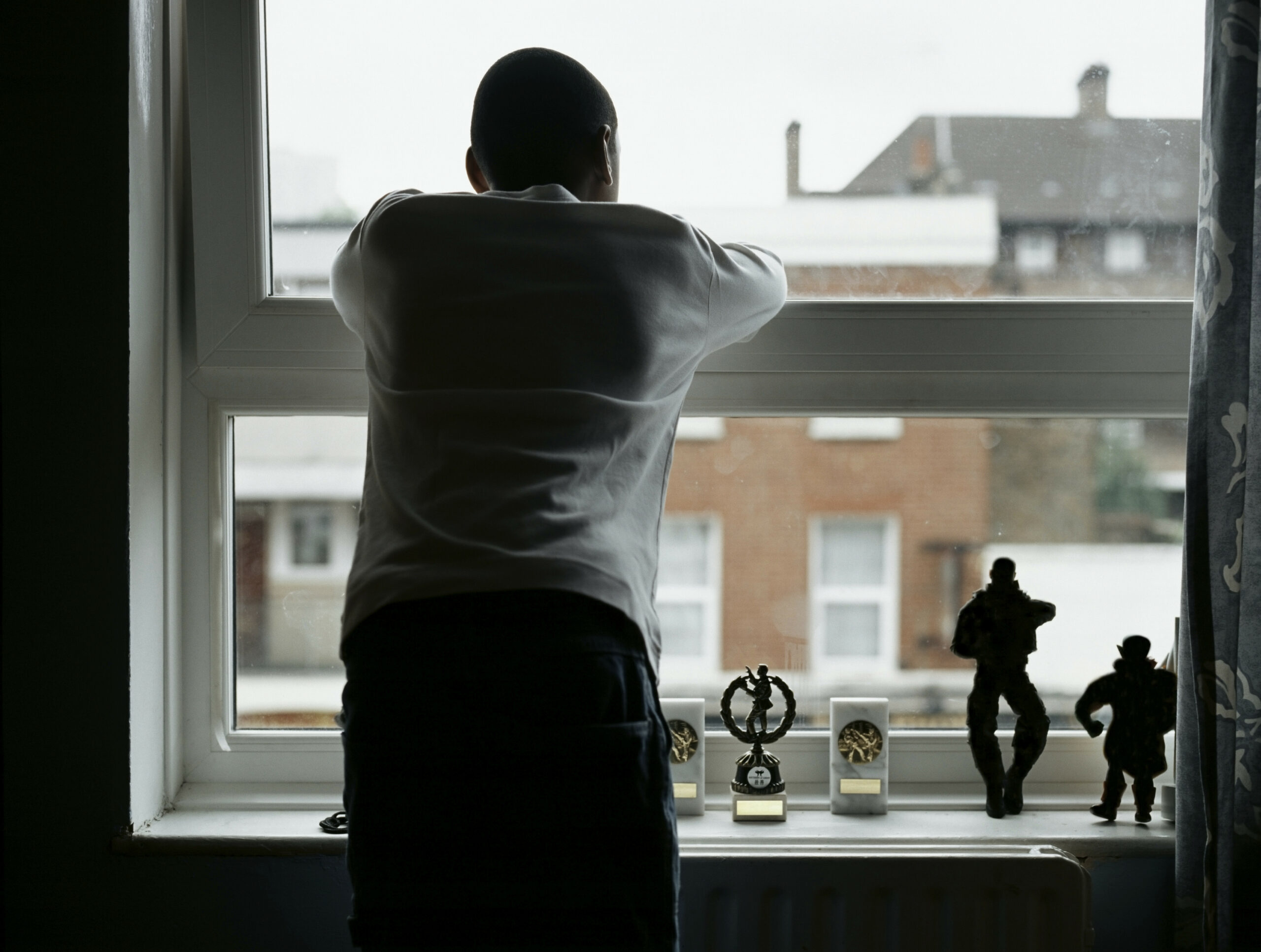 Personne en tenue d'intérieur, tenant une tasse de café, regardant pensivement par la fenêtre le monde extérieur.