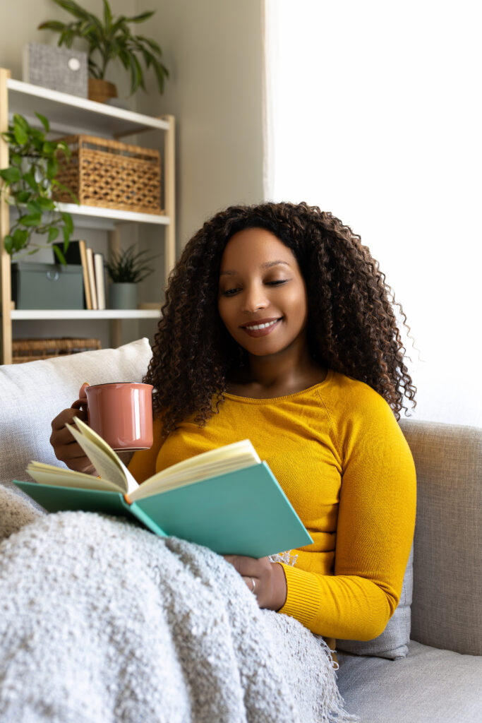 Personne lisant un livre avec un sourire léger chez elle, dans une atmosphère lumineuse et paisible.